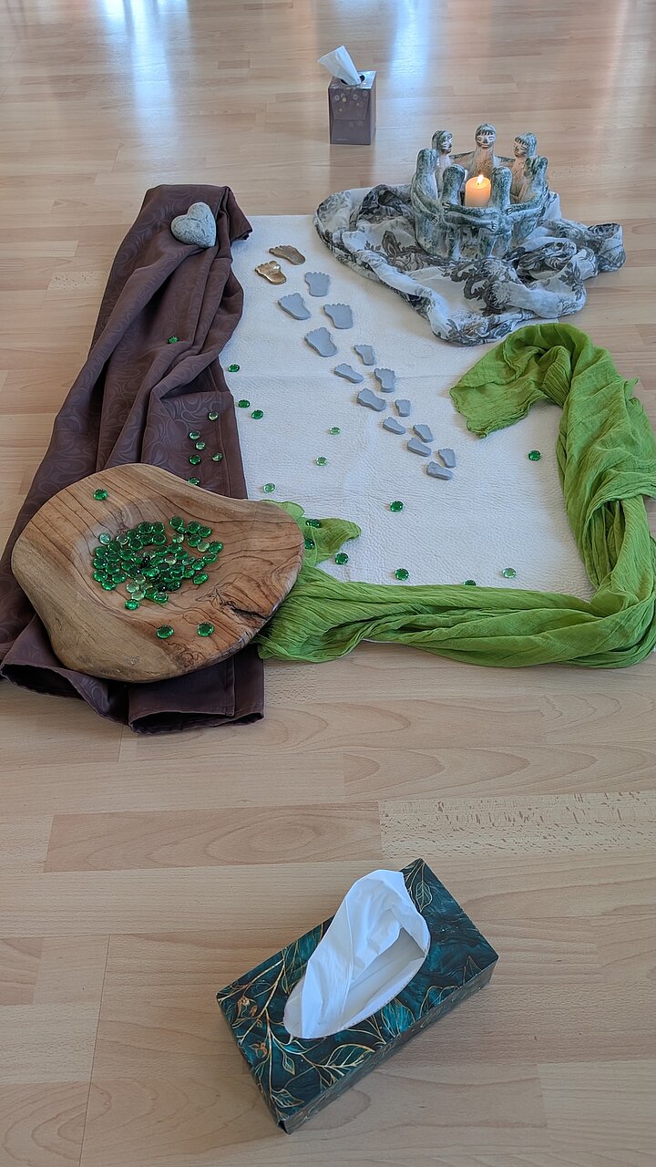 Symbolische Gestaltung aus dem Sterbebegleitseminar der AKADEMIE² mit Kerze, Fußabdrücken, Stoffen und Steinen