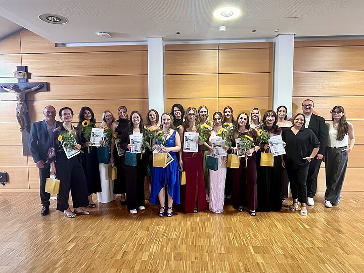 Die 16 Absolventinnen der OTA-Ausbildung mit Zeugnissen und Sonnenblumen, umrahmt von den Dozentinnen und Dozenten.