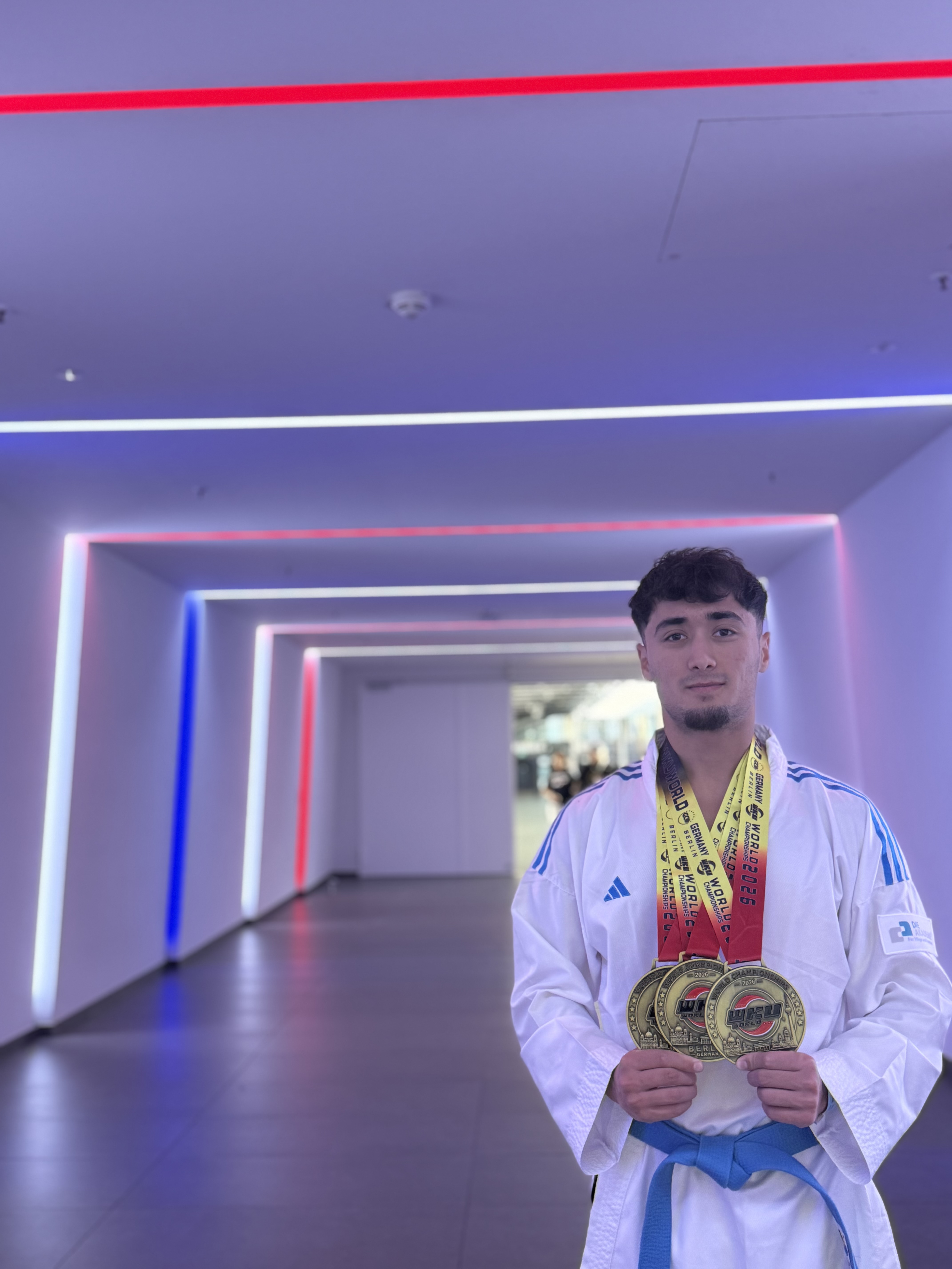 Dilshod Jaborov steht im Karateanzug mit seinen drei WM-Medaillen in Gold im Flur.